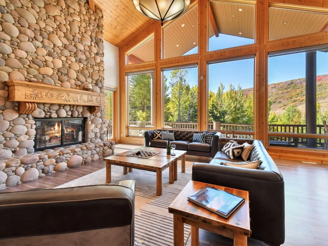 A spacious living room with seating, a stone fireplace, and large windows.