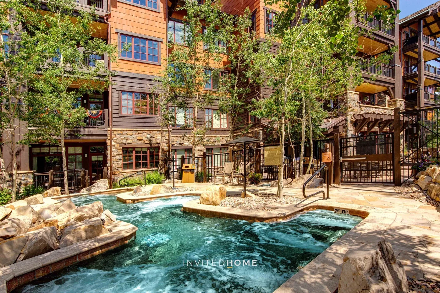 Una piscina al aire libre está junto a un patio ajardinado y un edificio de varios pisos.