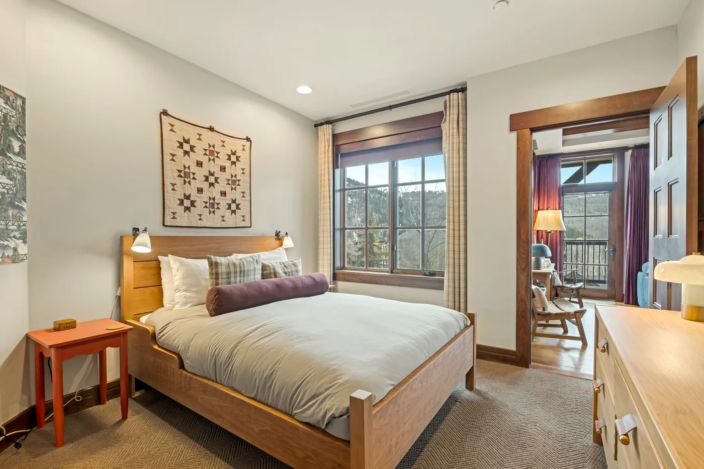 Un dormitorio con una cama de madera, un tapiz estampado y ventanas amplias.