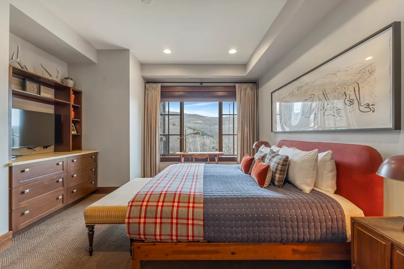 Un dormitorio con una cama frente a una ventana y un televisor sobre una cómoda.