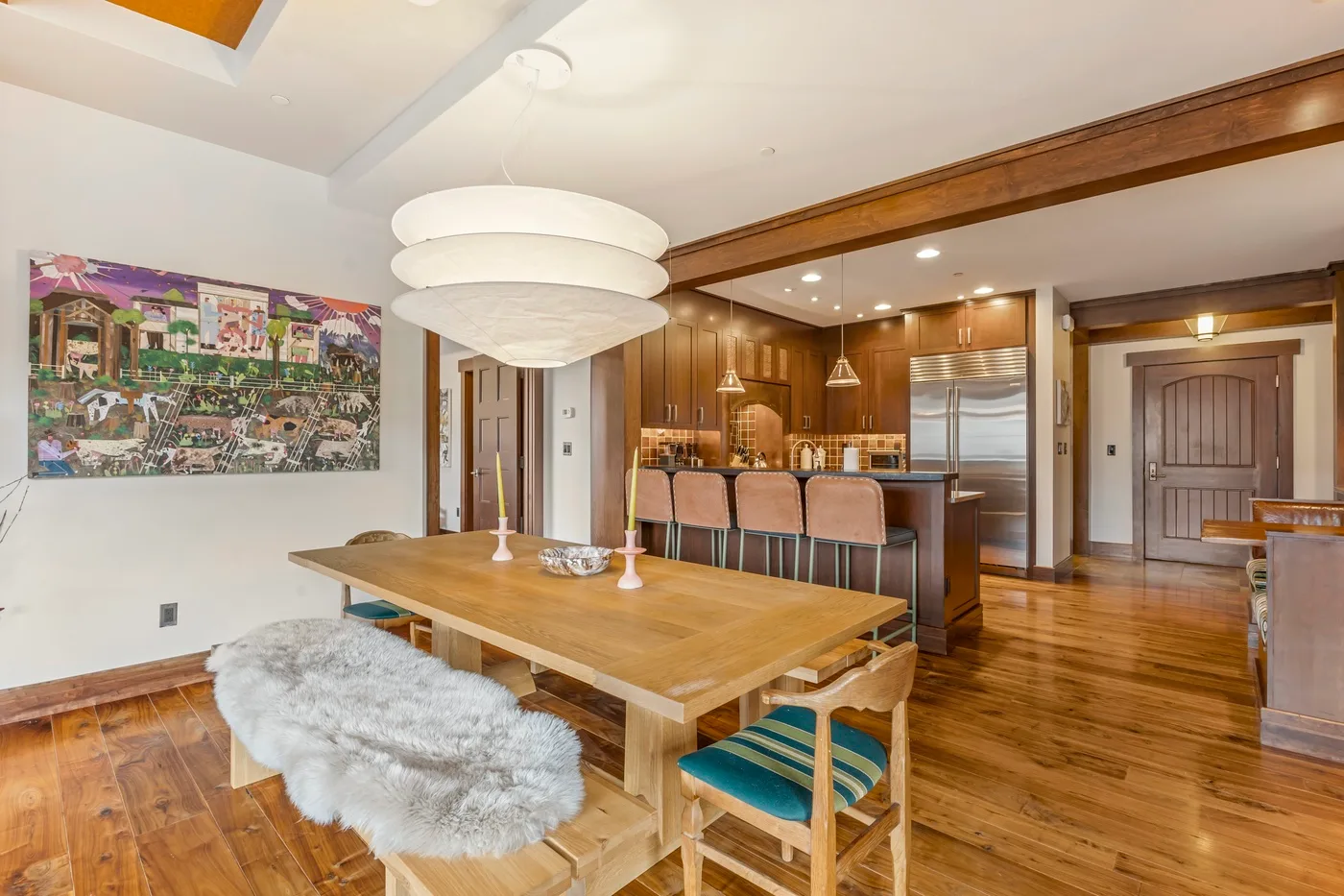 Un comedor comunica con la cocina, con una mesa de madera y arte colorido en la pared.