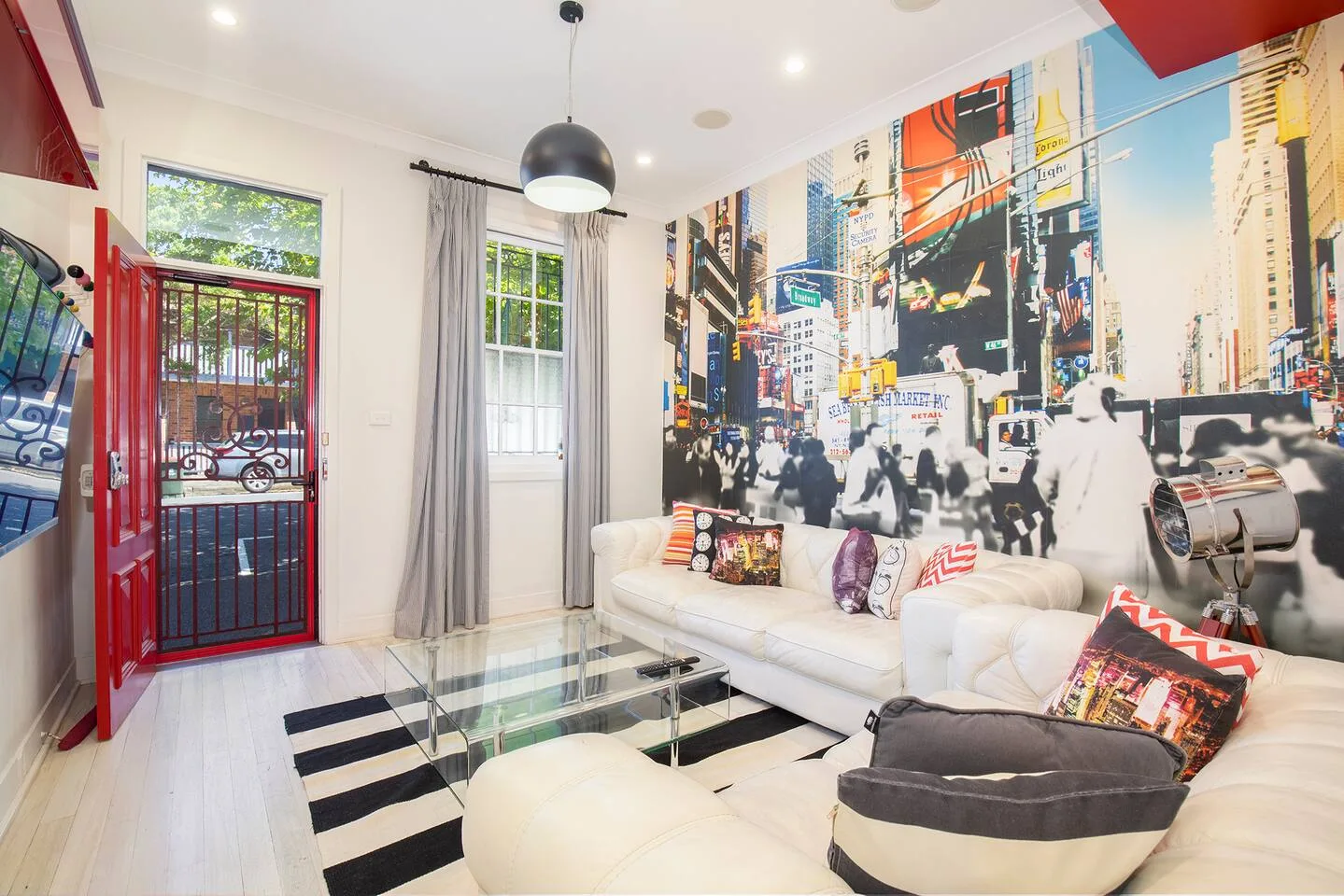A bright living room features white seating, a glass coffee table, and a colorful cityscape mural.