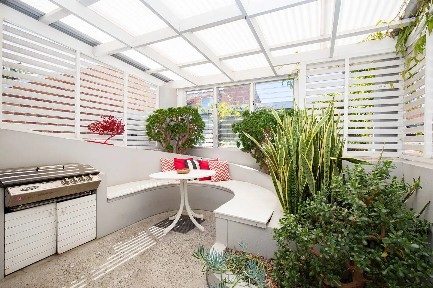 A covered patio has built-in curved seating and a barbecue.