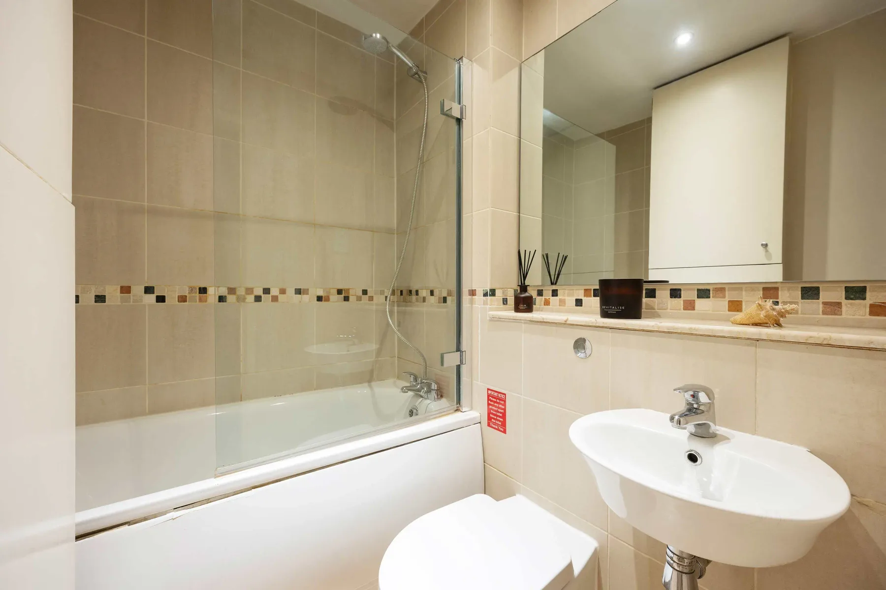 Un baño alicatado con bañera, mampara de ducha de vidrio y lavabo.