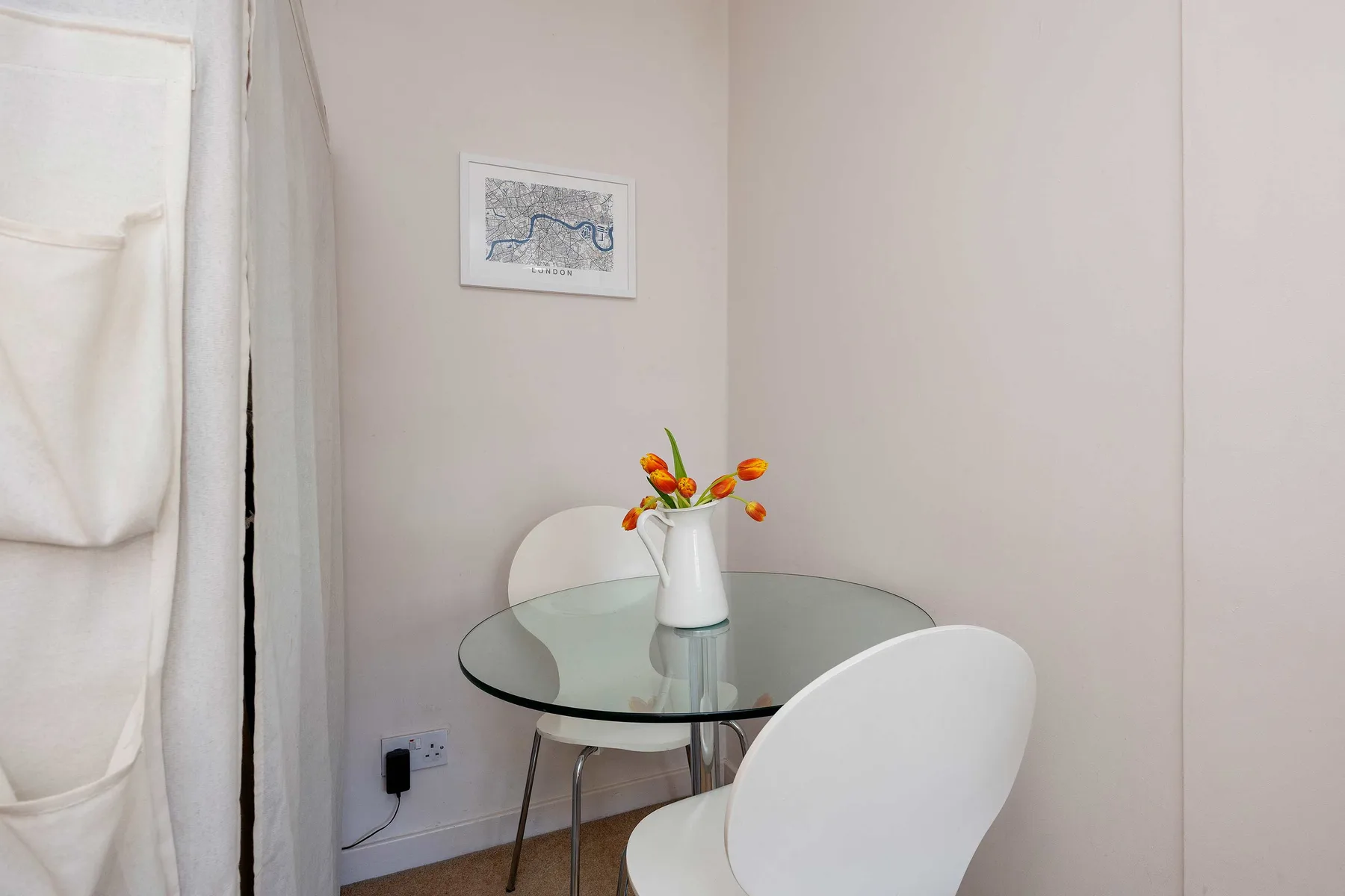 Un pequeño comedor con una mesa redonda de vidrio y flores.