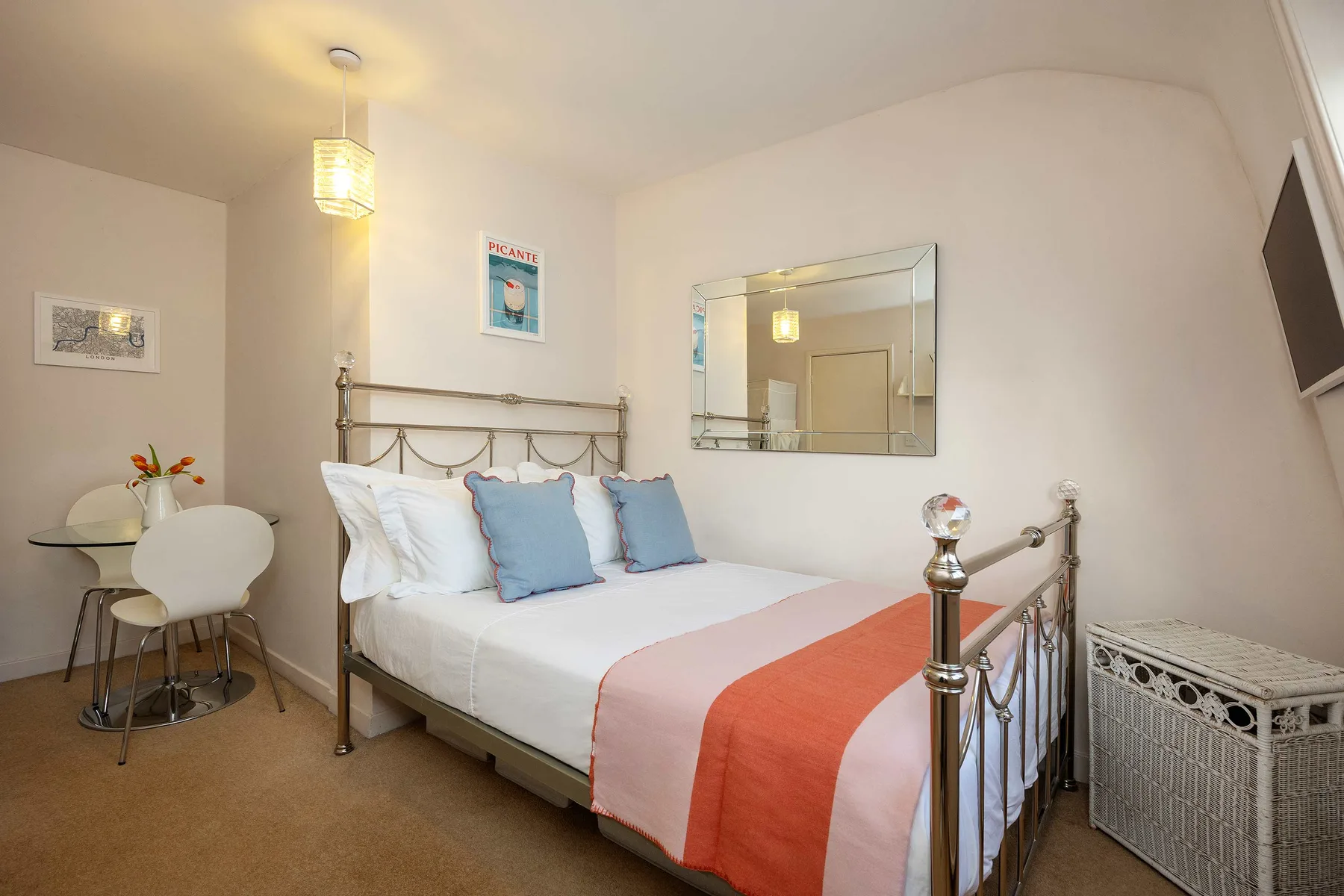 Un dormitorio con una cama bien tendida, almohadas azules y una manta color coral.