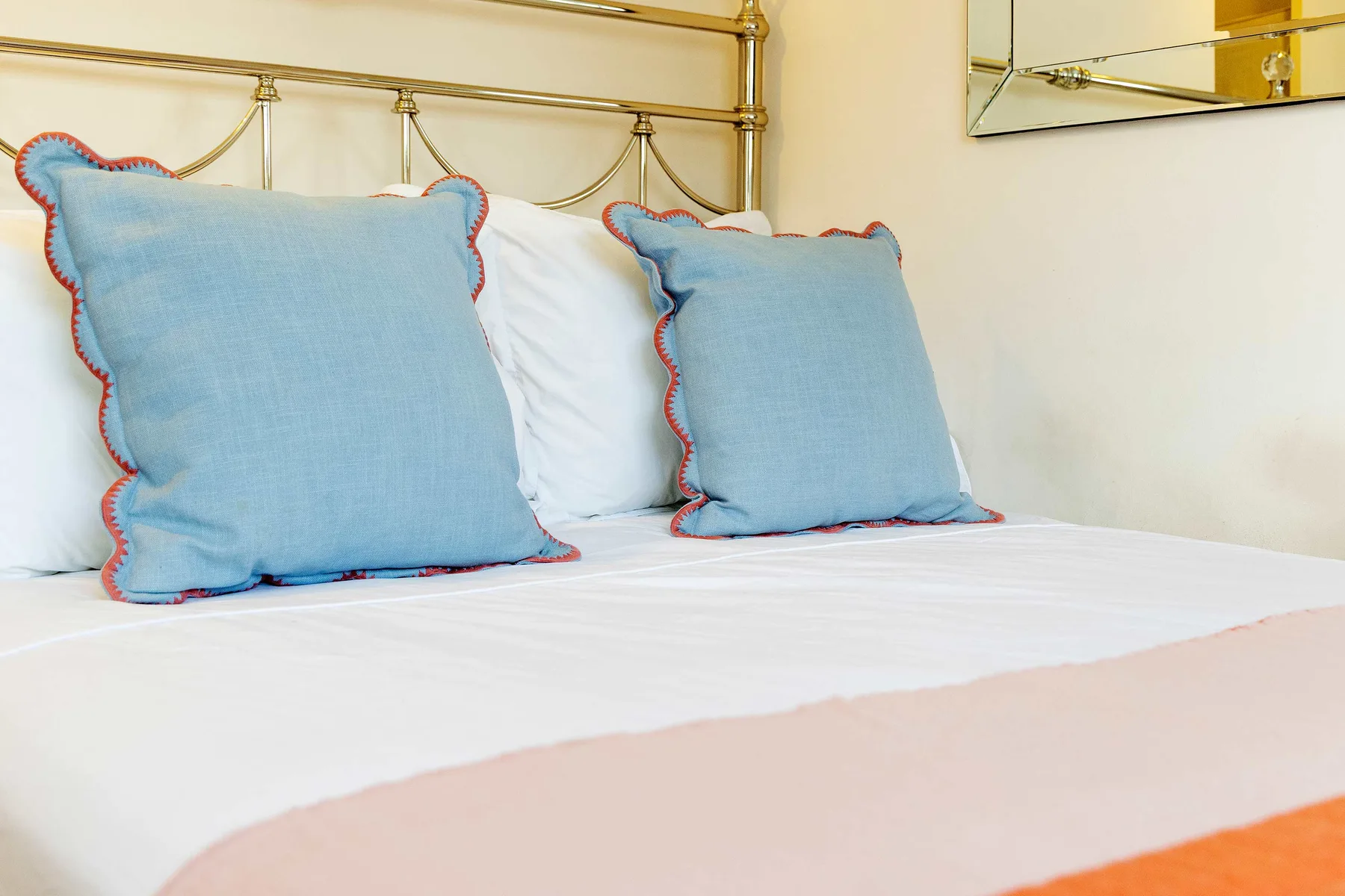 Una cama de dormitorio está tendida con ropa de cama blanca y cojines decorativos azules.