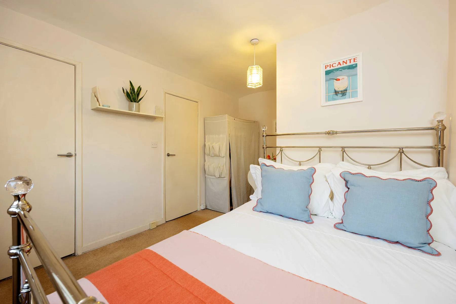 Un dormitorio con una cama de estructura metálica, almohadas azules y una colcha colorida.
