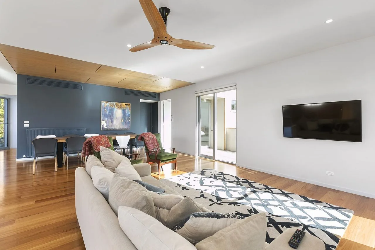 Una sala luminosa con asientos, una alfombra estampada y un televisor en la pared.