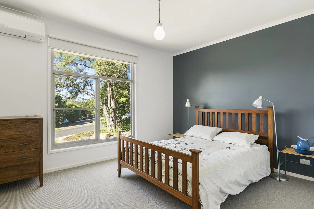 Un dormitorio con una cama de madera, ropa de cama blanca y una ventana grande.