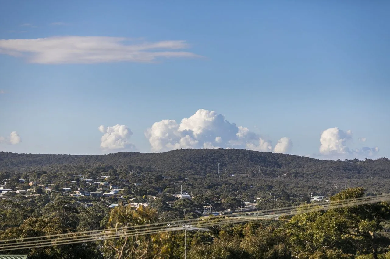 Un pueblo en una ladera se extiende bajo una cresta boscosa y un cielo azul.