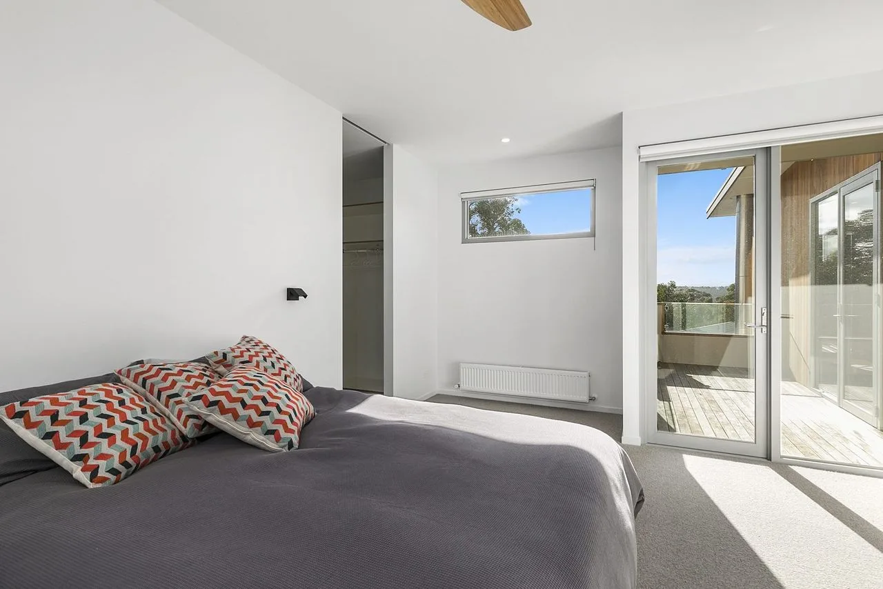 Un dormitorio luminoso con una cama junto a puertas corredizas de vidrio que dan a un balcón.