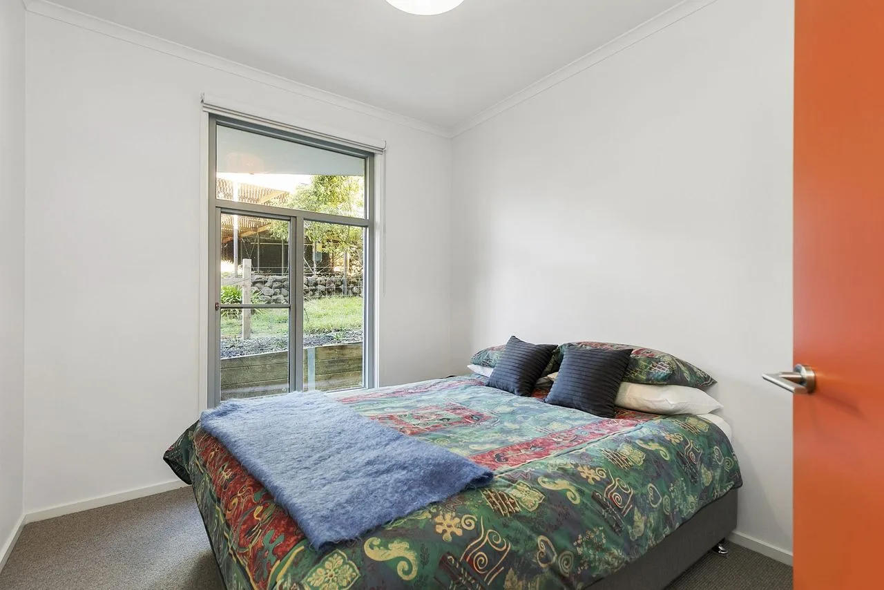 Un dormitorio con una colcha colorida y una ventana grande con vistas a la vegetación.