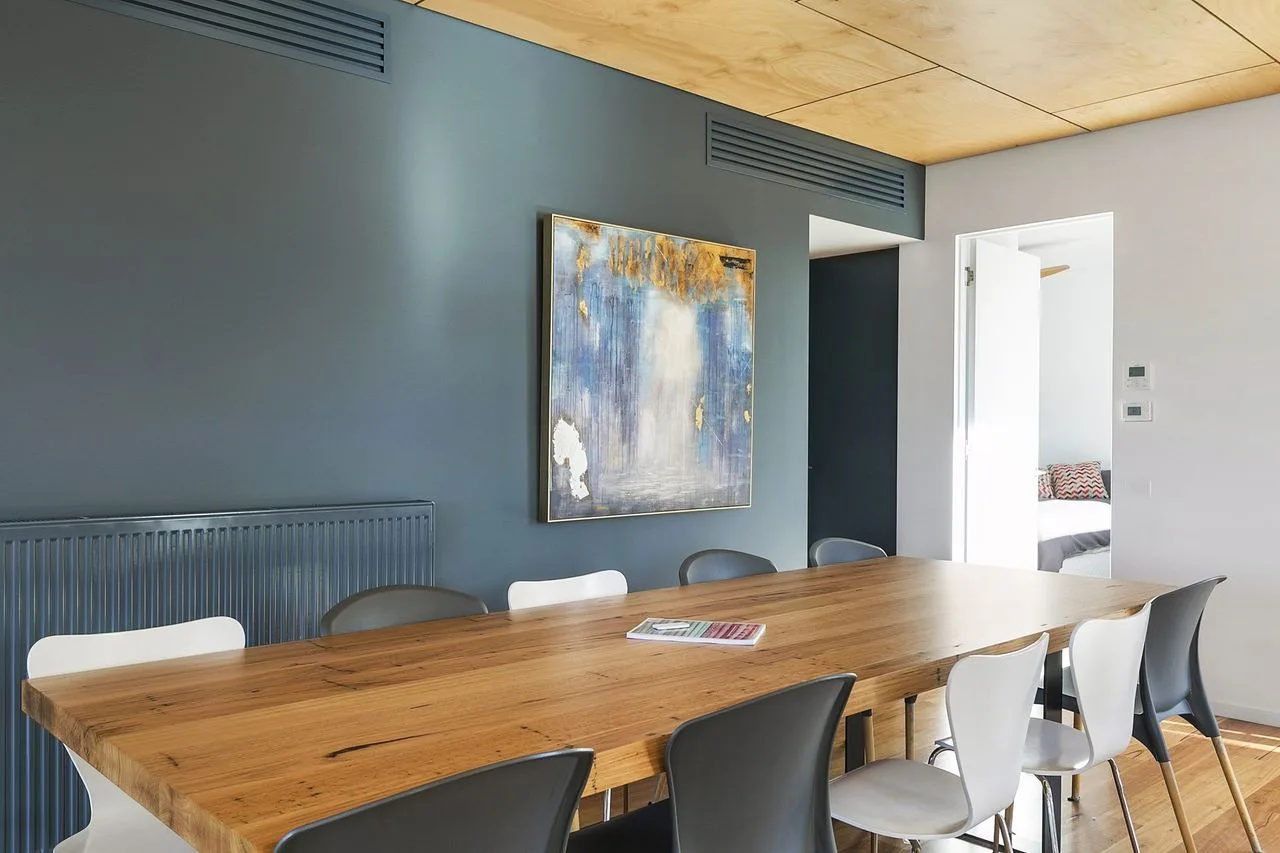 Comedor con una mesa larga de madera y sillas bajo una pintura abstracta.