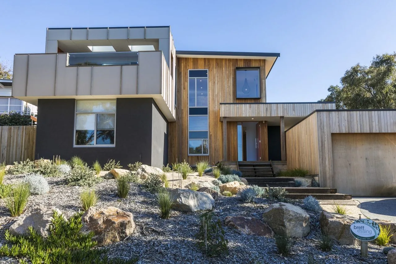 Exterior de una casa moderna con revestimiento de madera y un jardín rocoso.