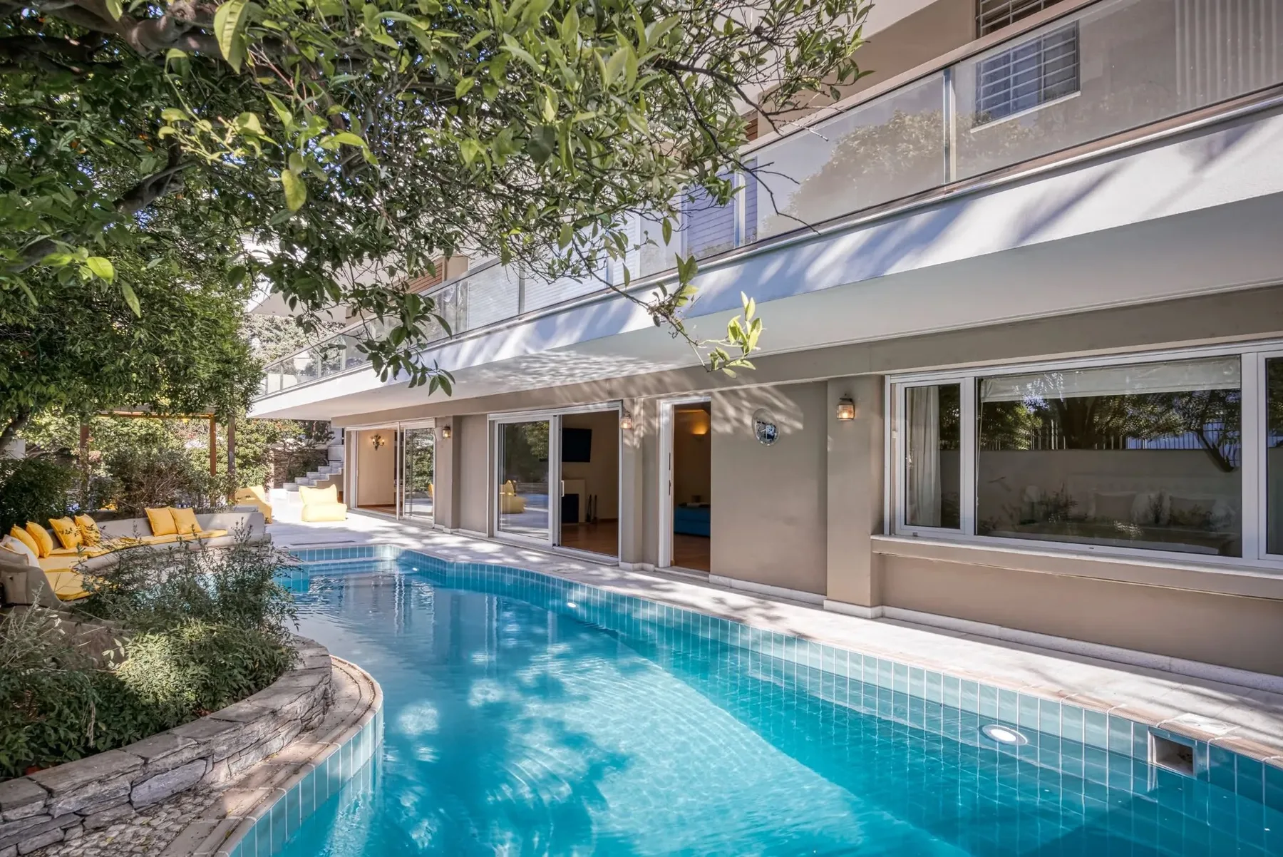A swimming pool runs alongside a modern house with large windows.