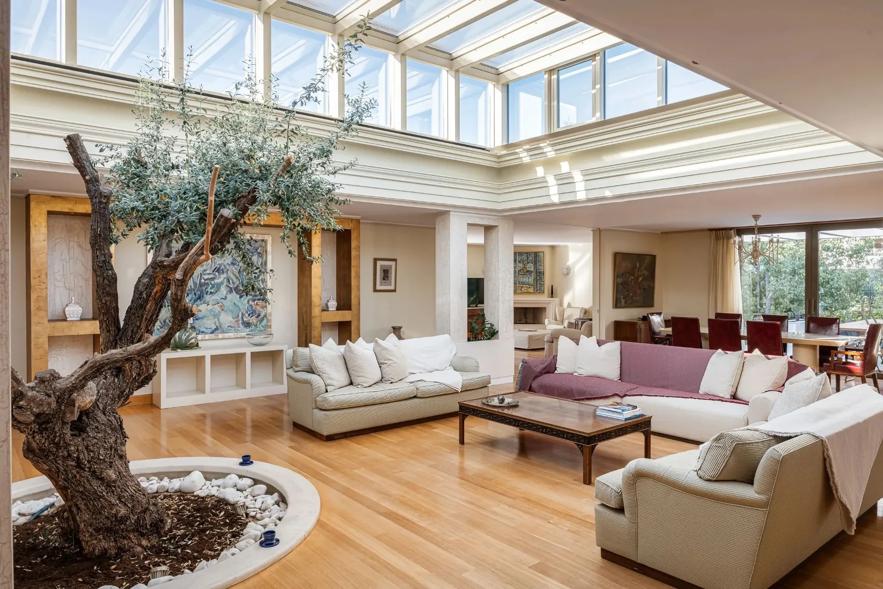 A bright living room with sofas arranged around a coffee table beneath a glass ceiling.