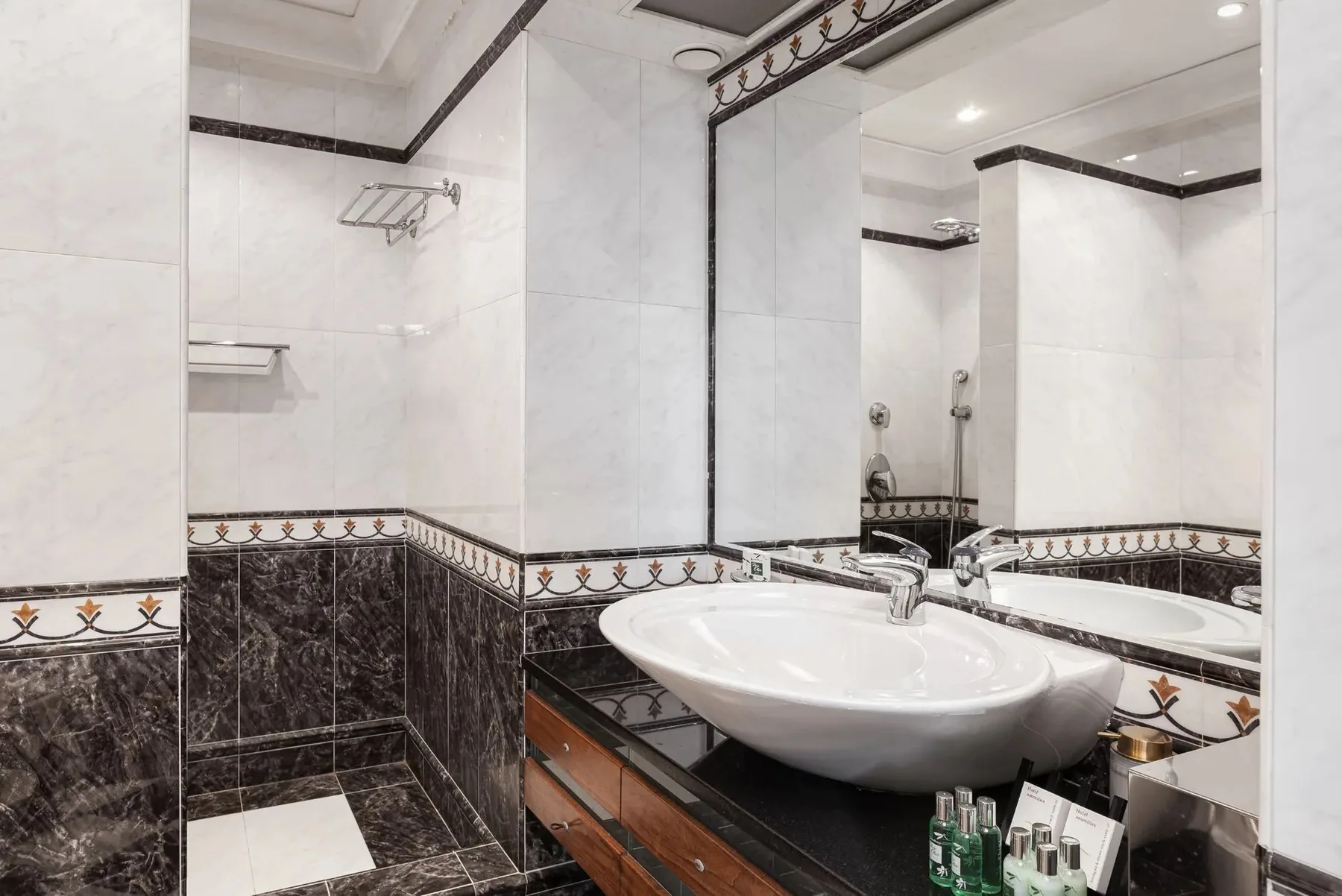 A bathroom with a sink, large mirror, and patterned tile trim.