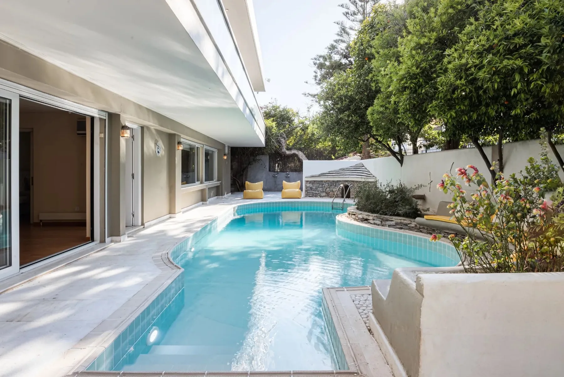 An outdoor swimming pool beside a modern house and landscaped garden.