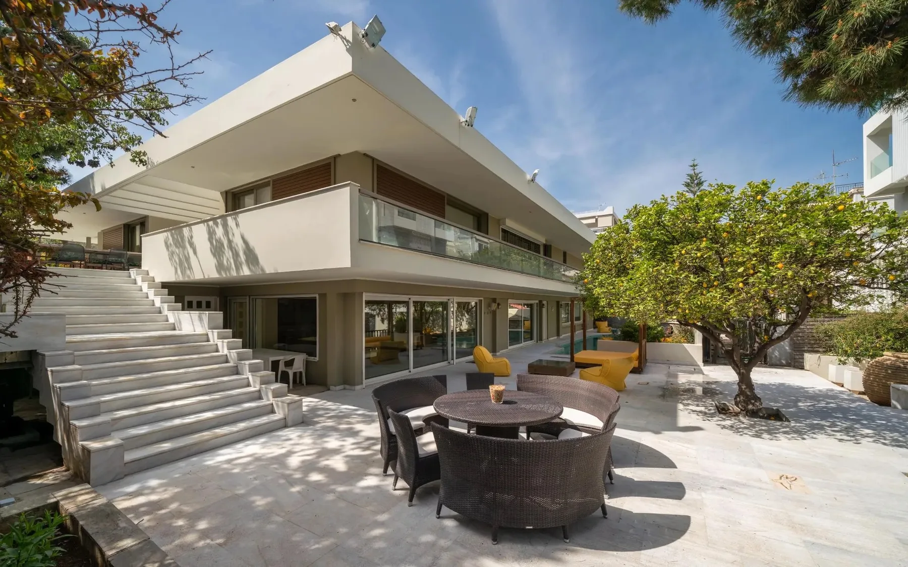 Modern house with a broad terrace, outdoor seating, and trees.