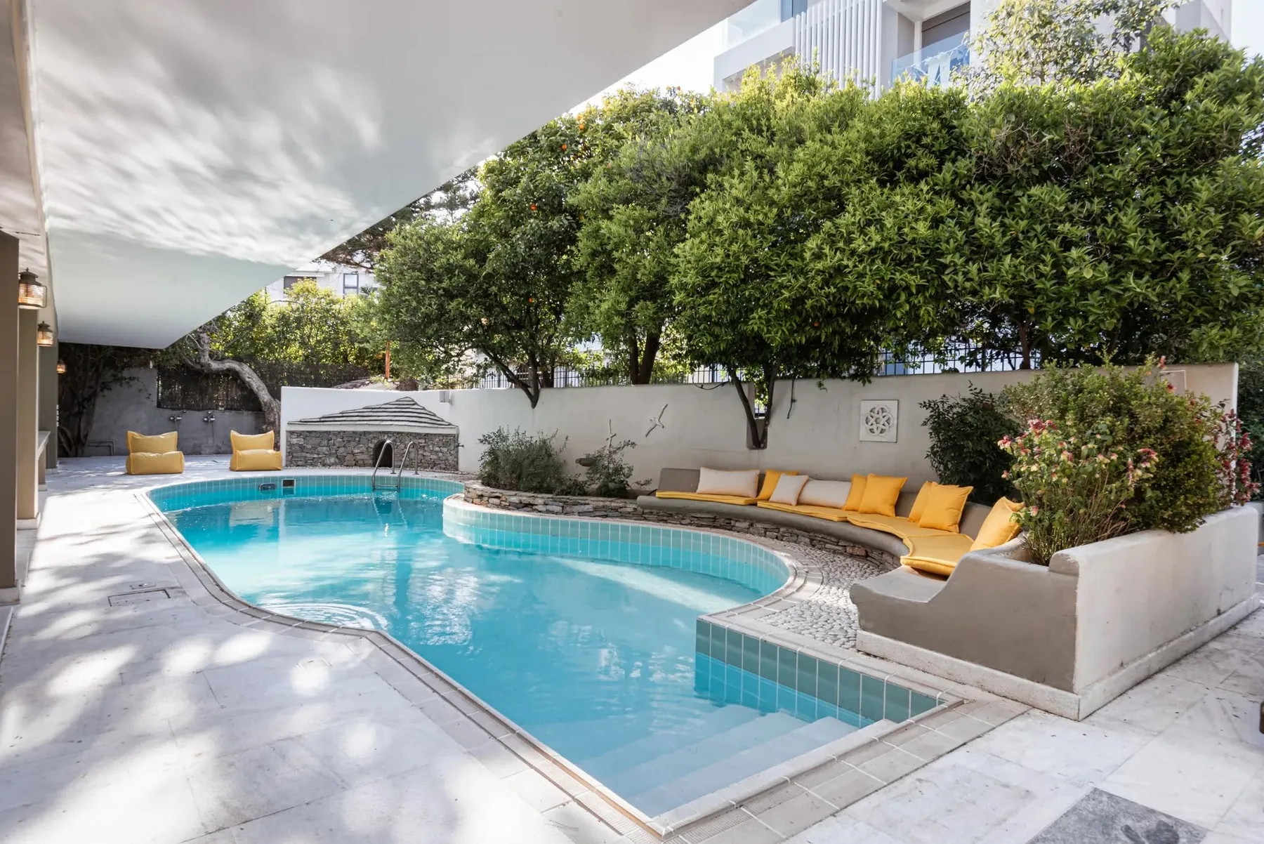An outdoor swimming pool is surrounded by seating and leafy trees.