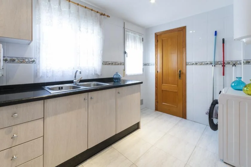 Un cuarto de servicio luminoso con azulejos, una encimera larga, fregadero y puerta de madera.