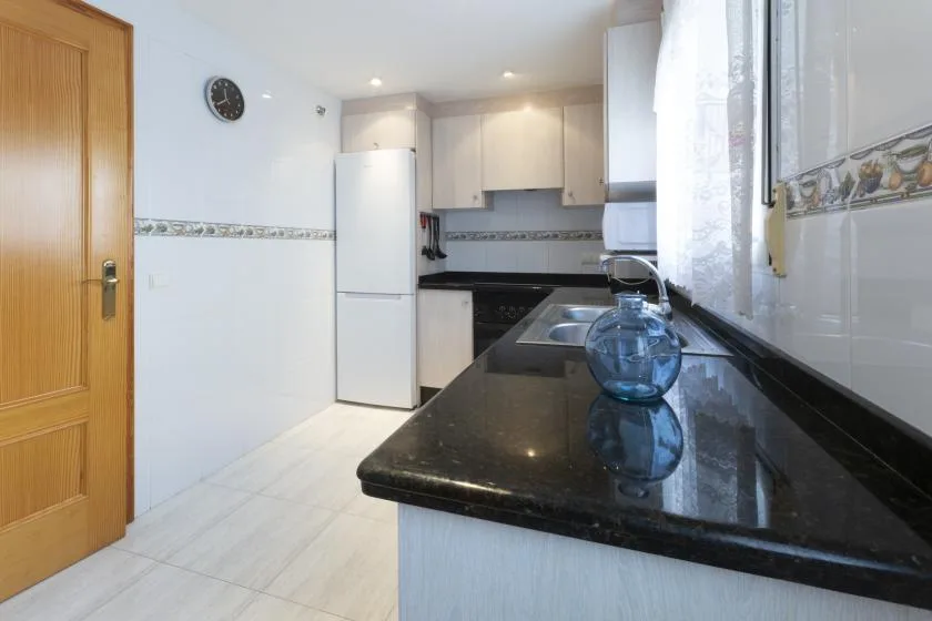 Una cocina con gabinetes claros, un refrigerador y una encimera oscura.