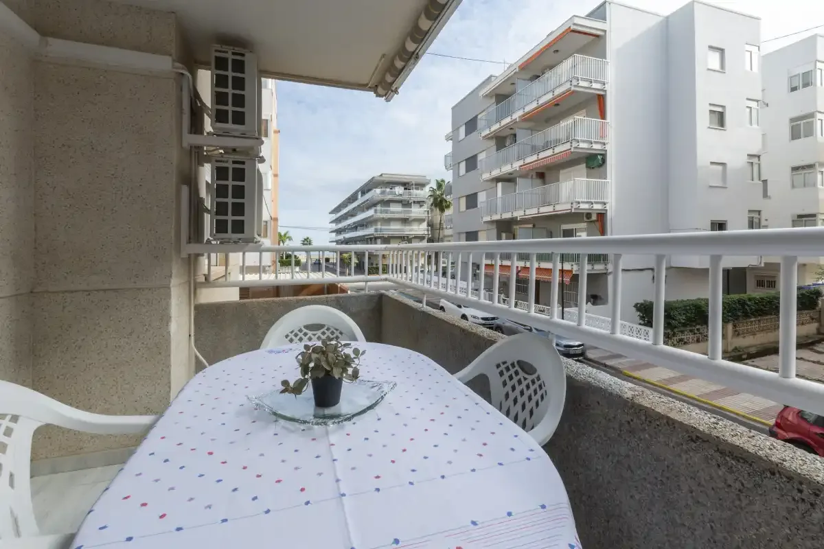 Una zona de estar en un balcón con una mesa redonda da a edificios de apartamentos cercanos.
