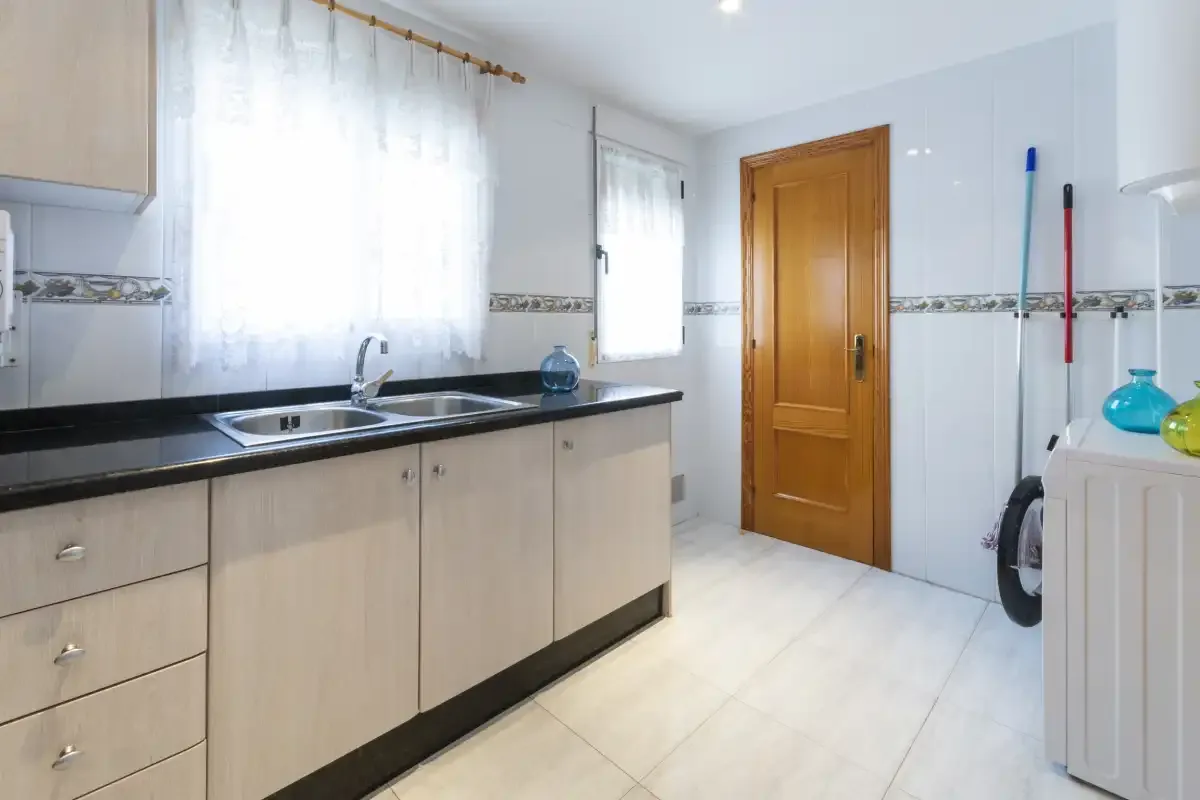 Una cocina luminosa con una encimera larga, fregadero y puerta de madera.