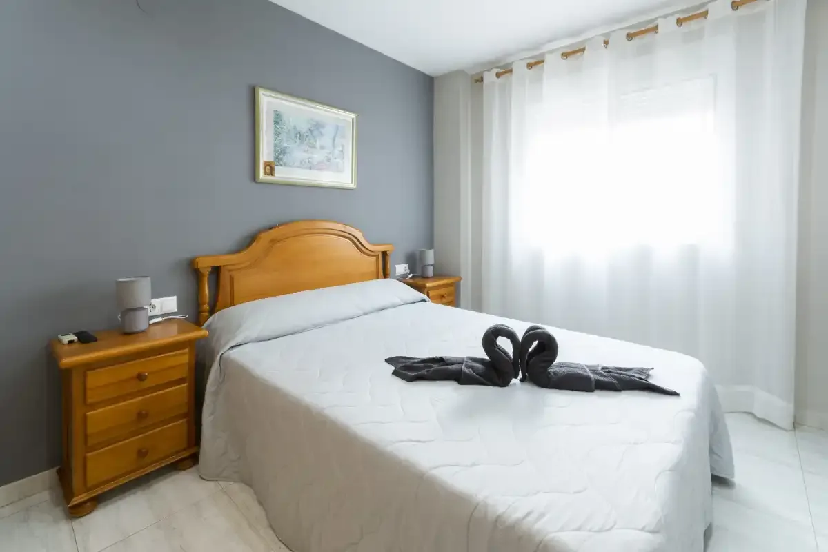 Dormitorio con una cama bien hecha, mesitas de noche y cortinas translúcidas.