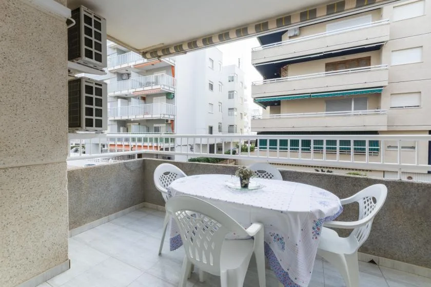 Zona de comedor en un balcón, con una mesa redonda y sillas frente a edificios de apartamentos.