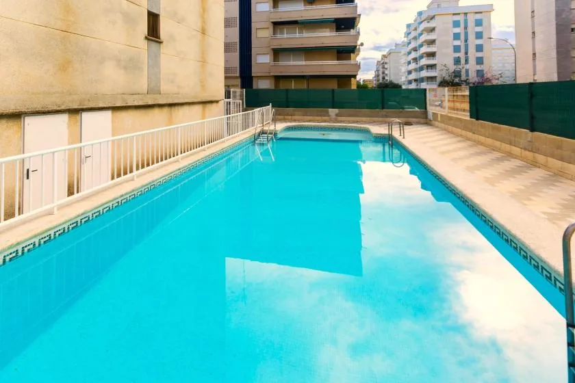 Una piscina al aire libre está junto a una terraza pavimentada y edificios de apartamentos.