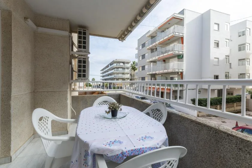 Comedor en un balcón con una mesa y asientos blancos frente a edificios de apartamentos.