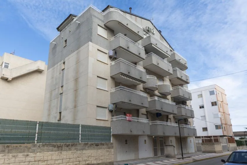 Un edificio de apartamentos de varios pisos con balcones salientes bajo un cielo azul.