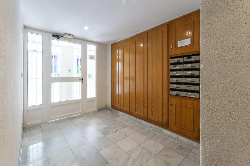 Una entrada luminosa con una puerta de vidrio y buzones de madera.