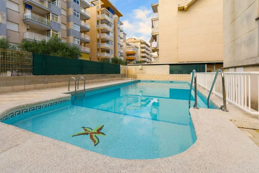 Una piscina rodeada de edificios de apartamentos tiene un mosaico colorido en el fondo.