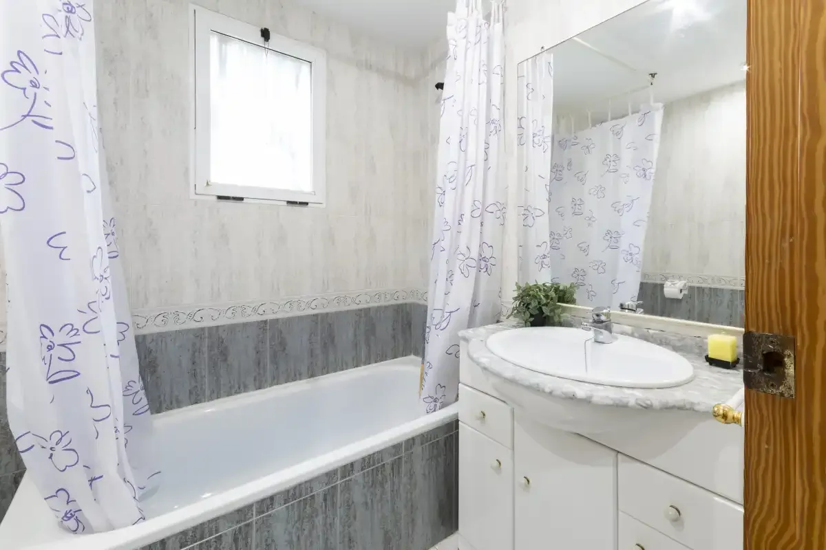 Un baño con bañera, cortina de ducha y lavabo bajo un espejo grande.