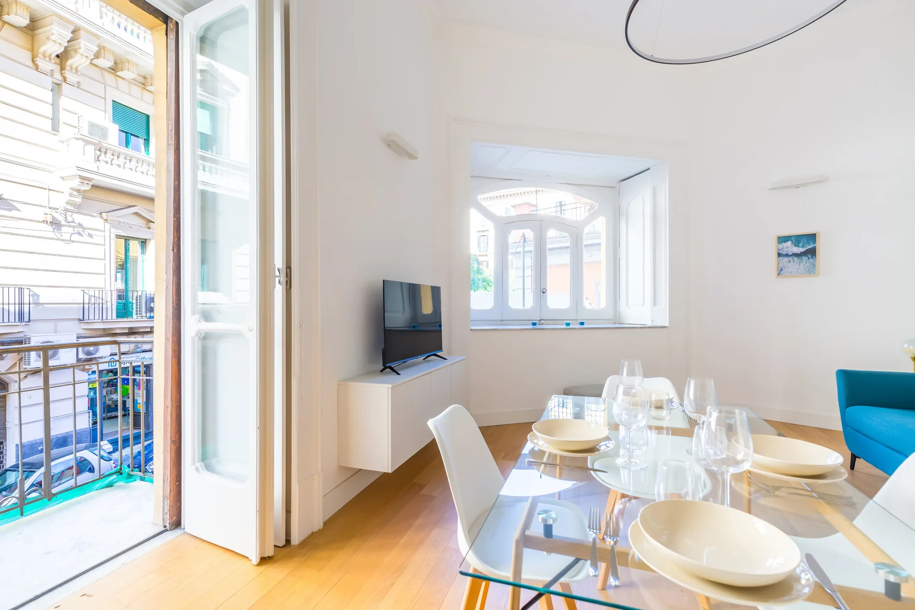 A bright dining area with a glass table set beside open windows.