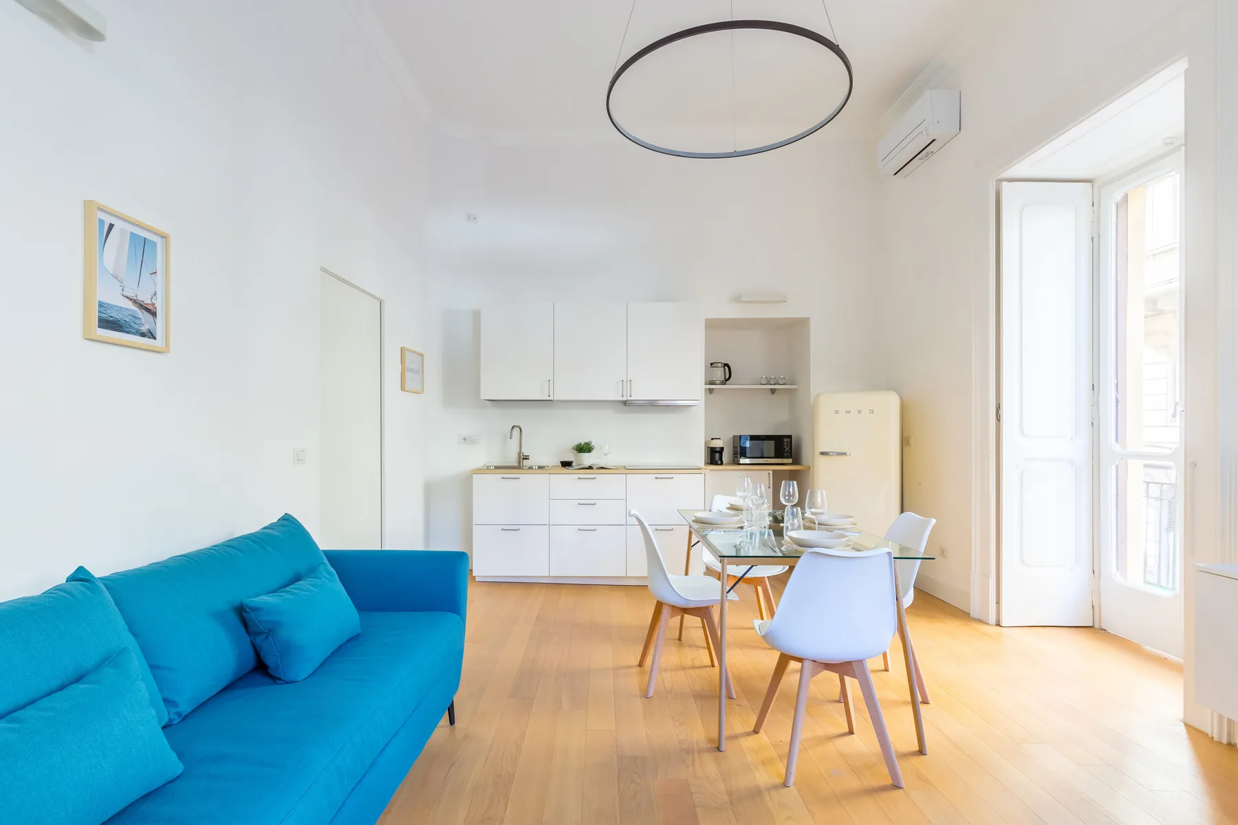 A bright living and dining area with blue seating, a table, and large windows.