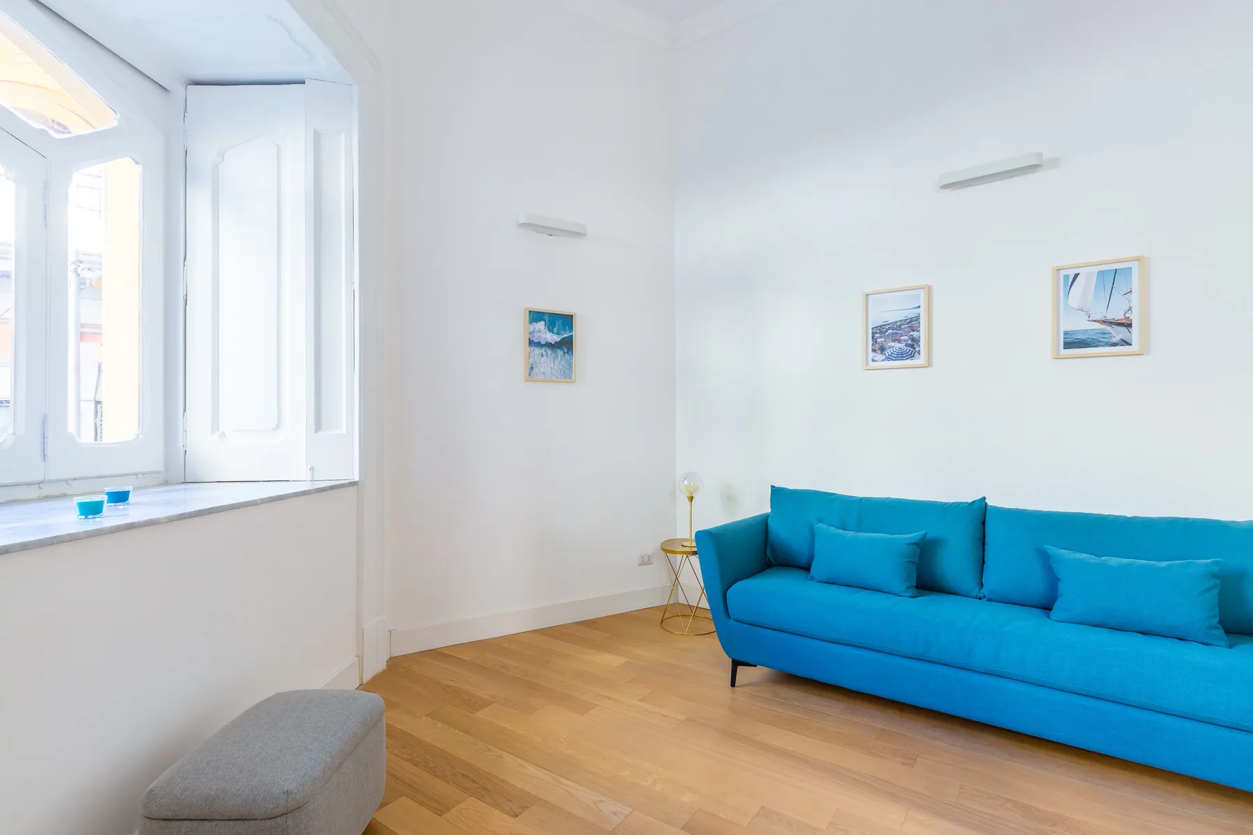 A bright living room with a blue sofa, framed pictures, and a large window.