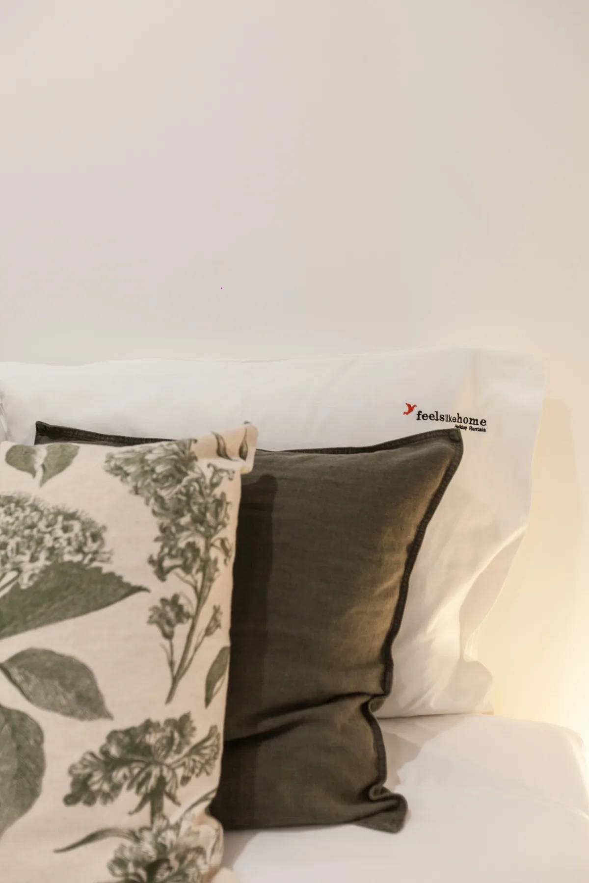 A bed with white bedding and patterned and dark decorative pillows.