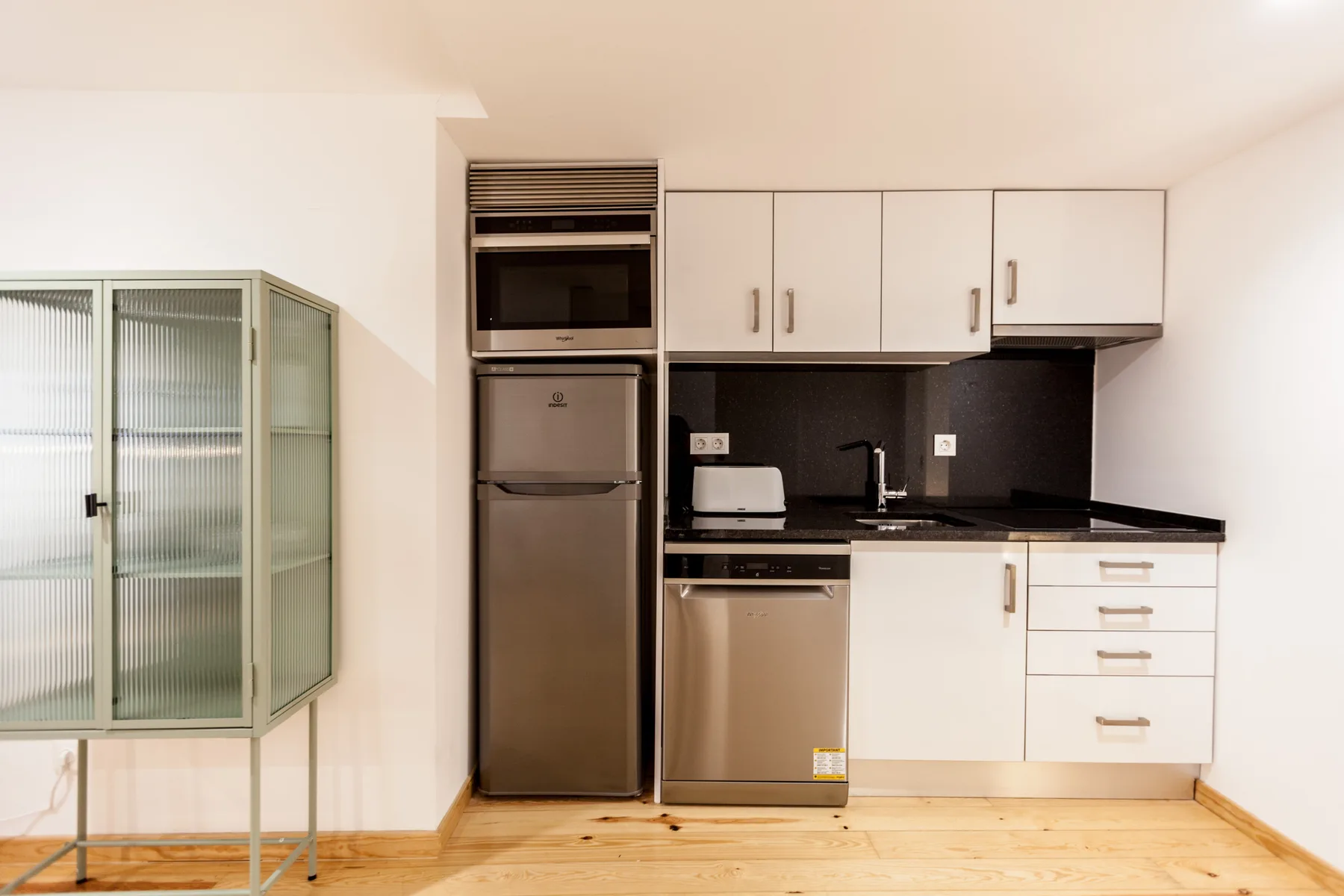 A compact kitchen with white cabinets, dark backsplash, and wood flooring.
