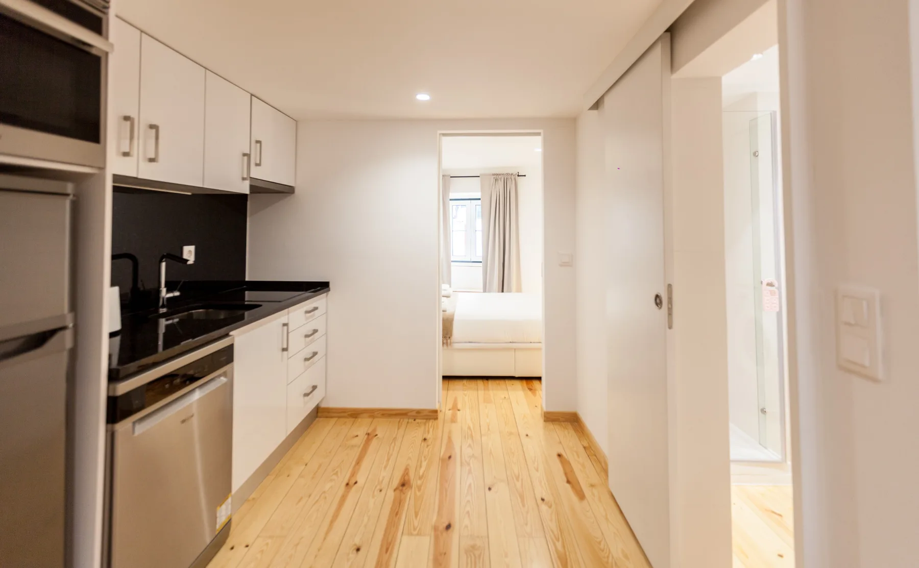 A compact kitchen opens onto a bright room with a bed visible beyond.