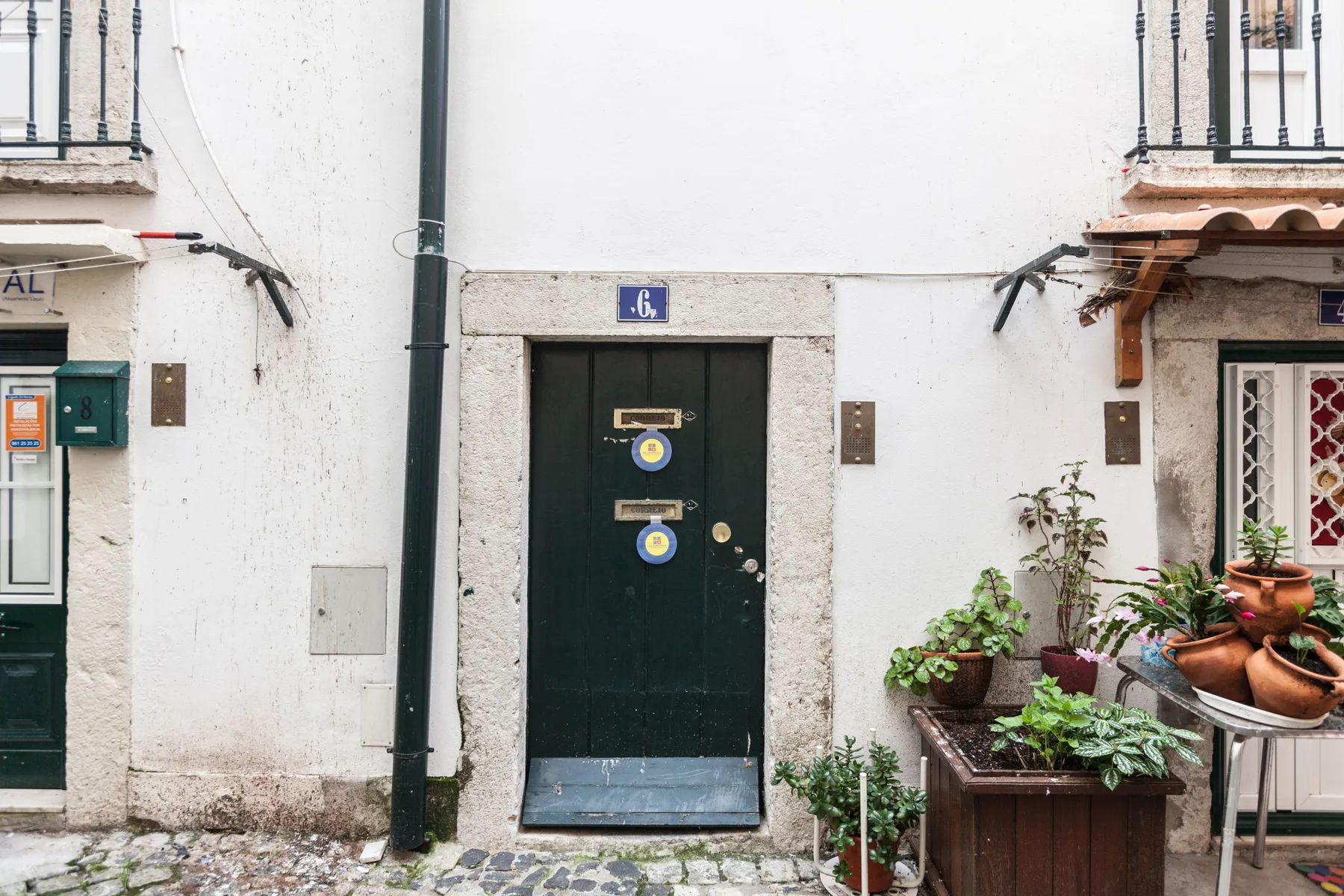 A dark green entrance door is set in a white exterior wall beside potted plants.