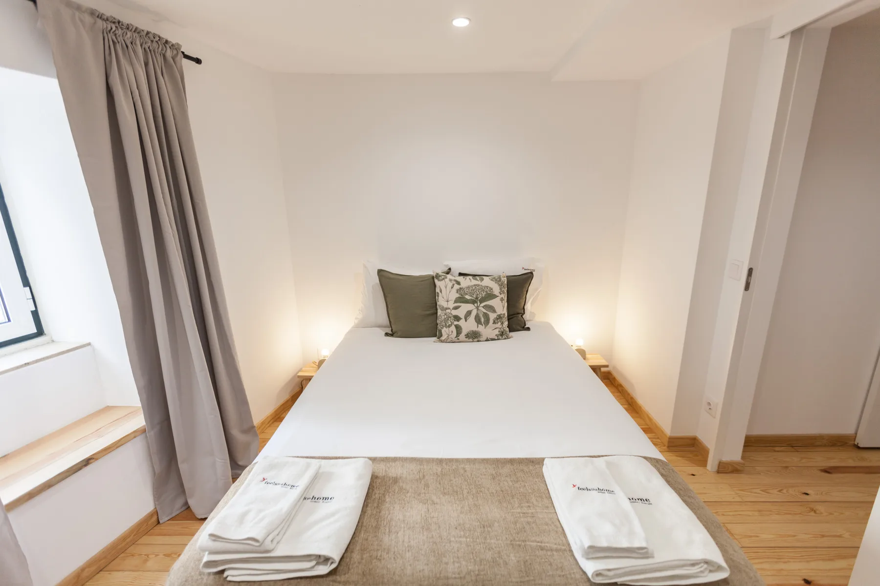 A bedroom with a neatly made bed and a window beside gray curtains.