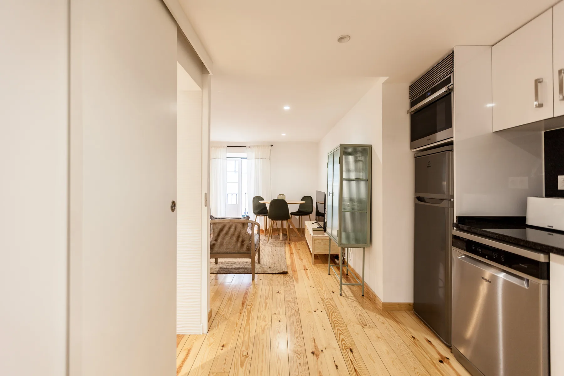 A bright apartment interior with a kitchen opening onto a dining area.