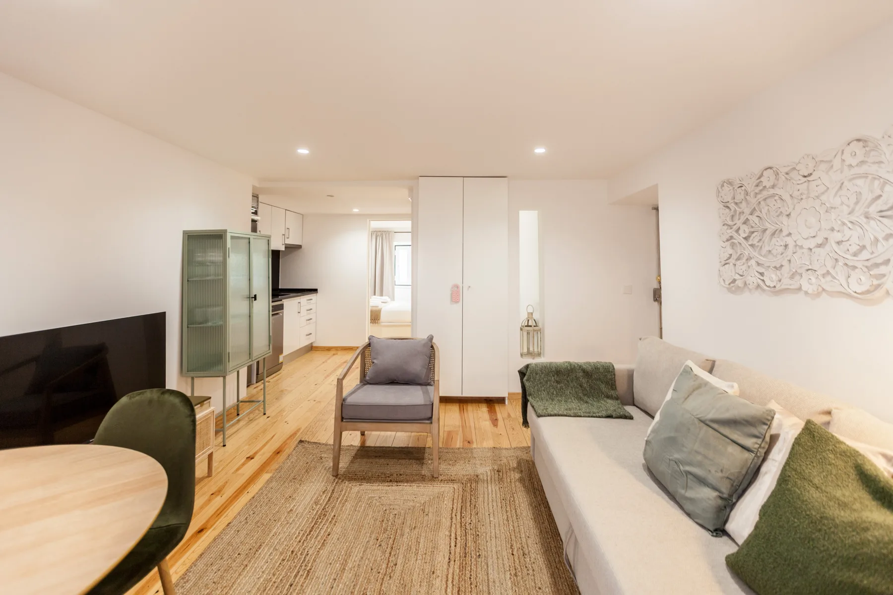 A bright living room with seating, a television, and an adjoining kitchen.