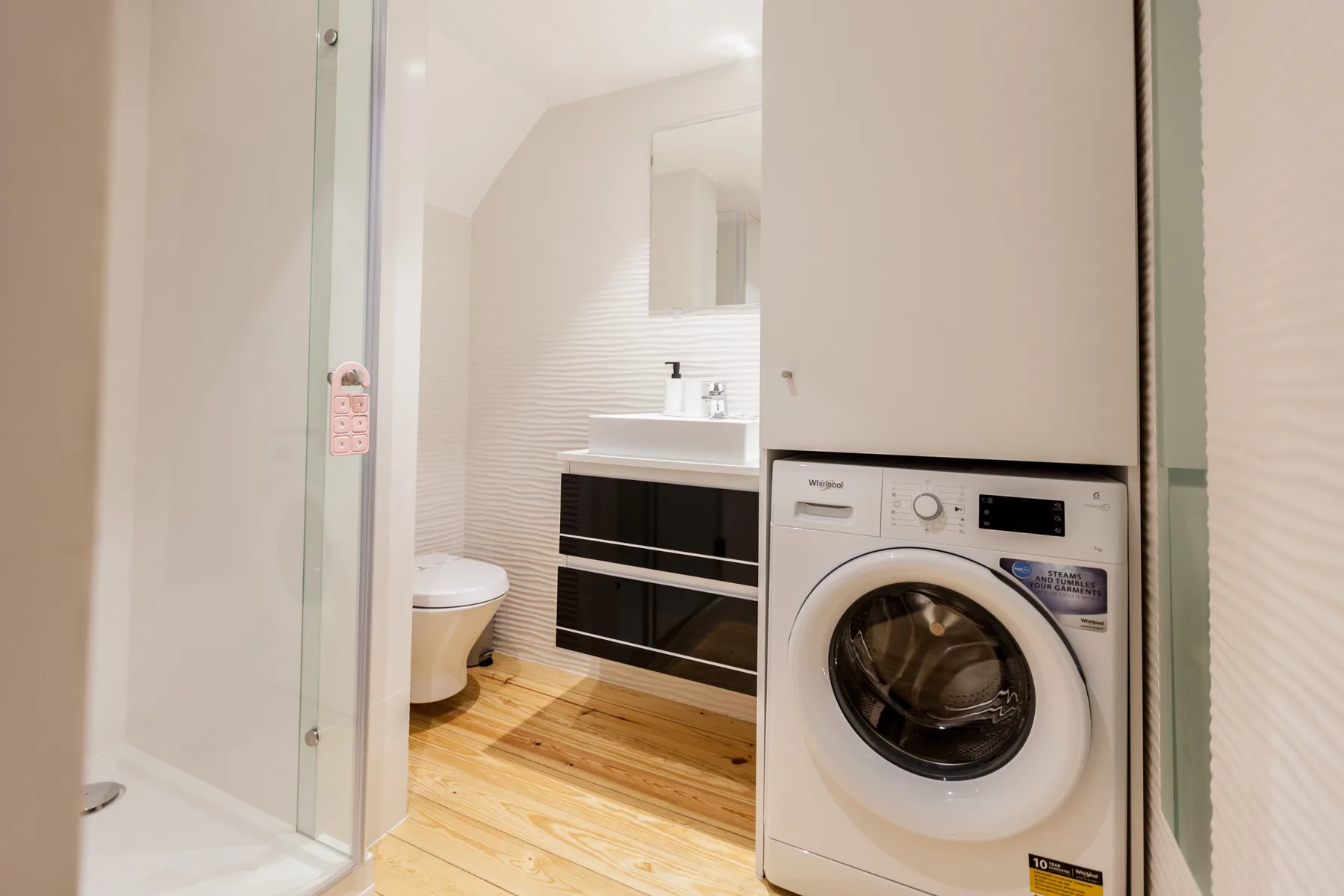 A bathroom with a washing machine beside the sink and shower.