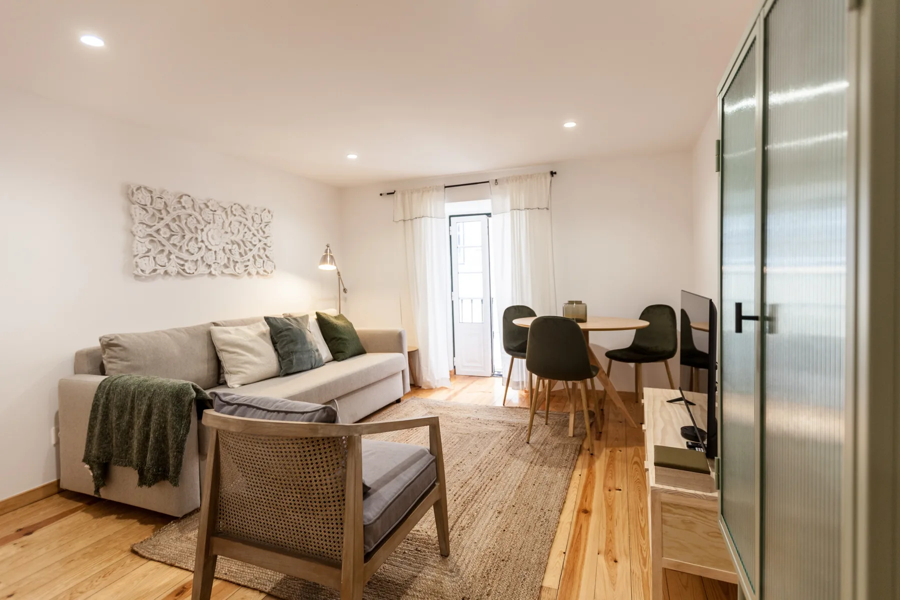 A bright living and dining area with seating, a table, and a balcony door.