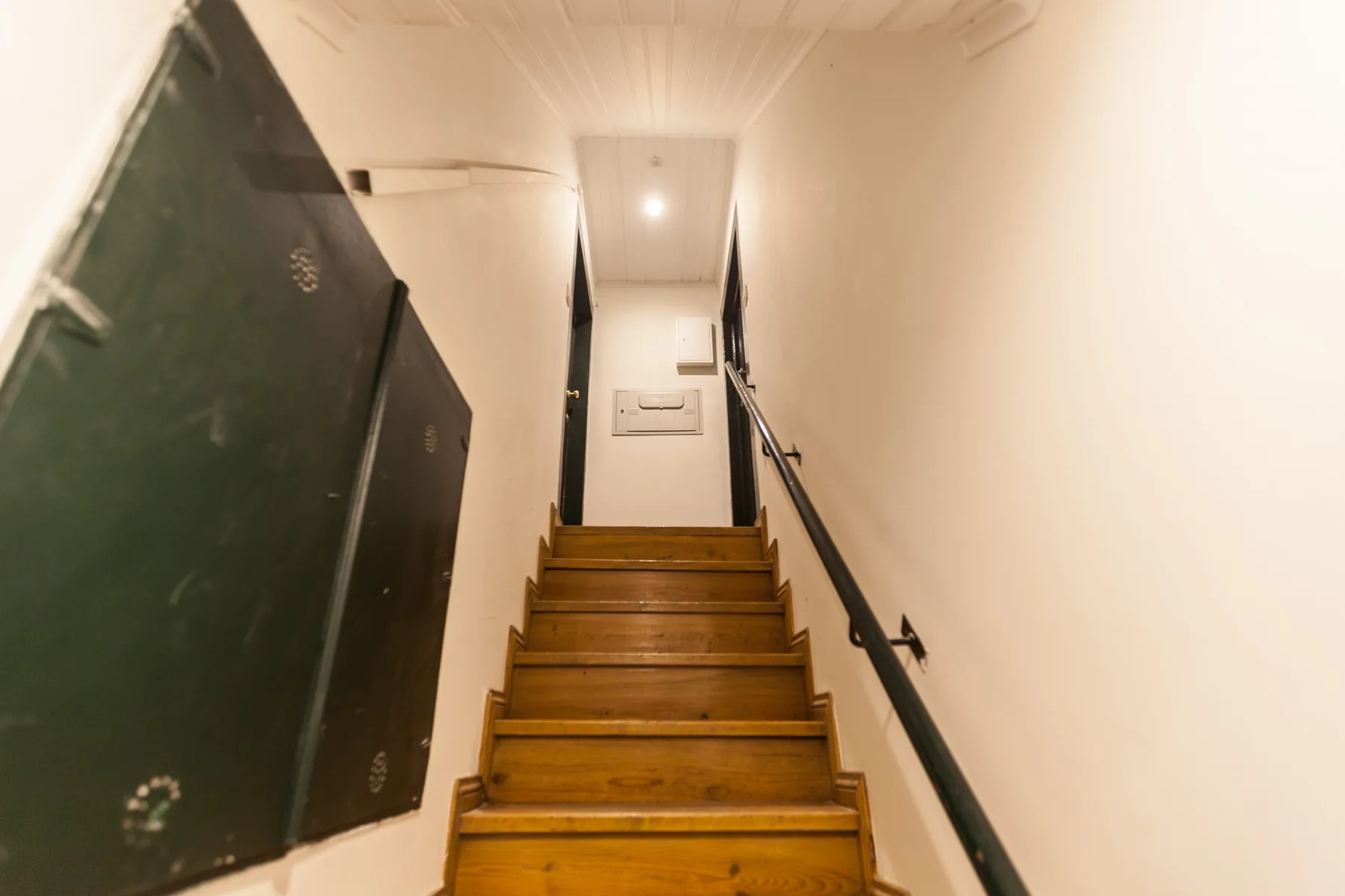 A narrow indoor staircase with wooden steps and a black handrail.
